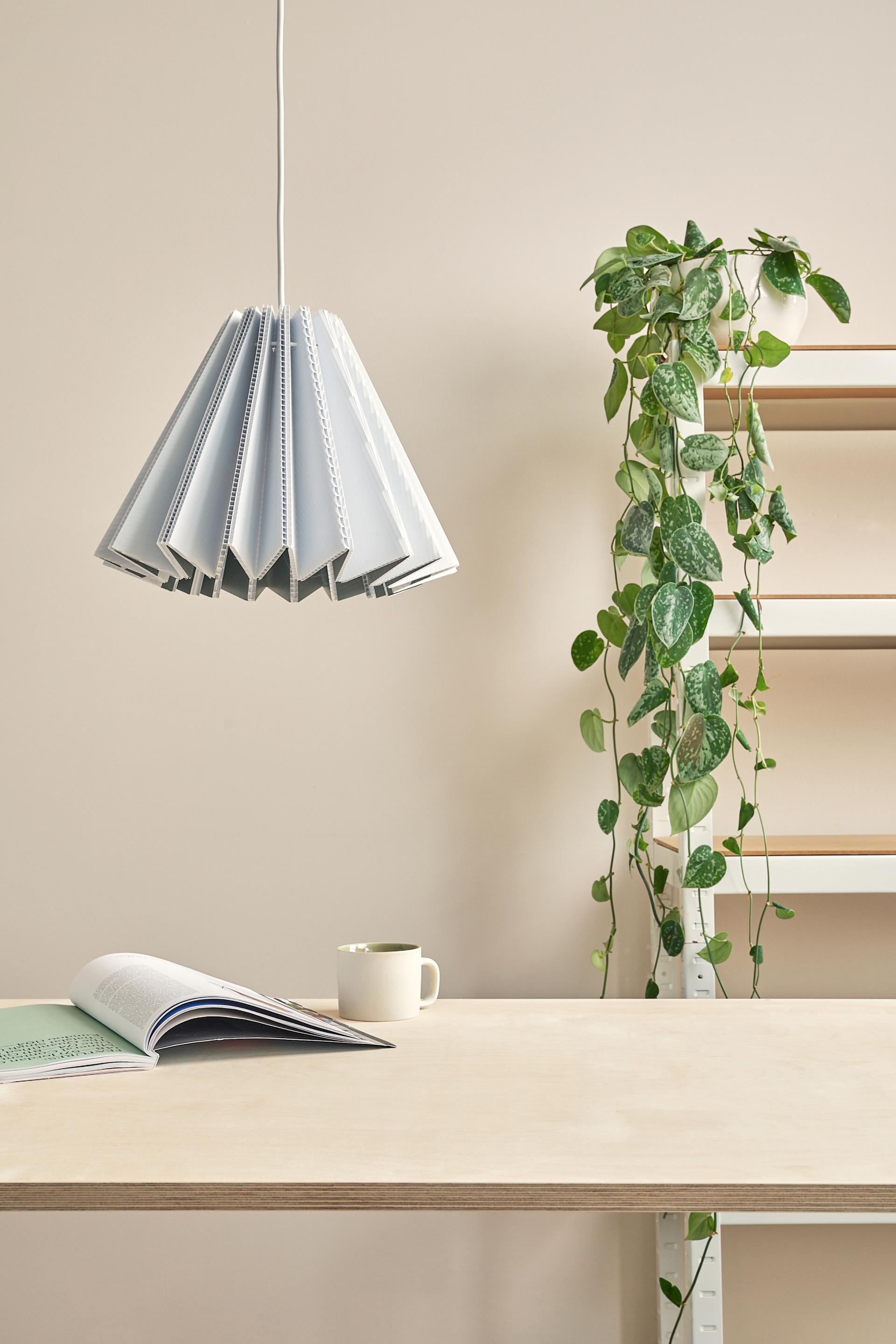Sustainable sculptural lampshade by Tabitha Bargh, hanging above a wooden table with a plant and open book.