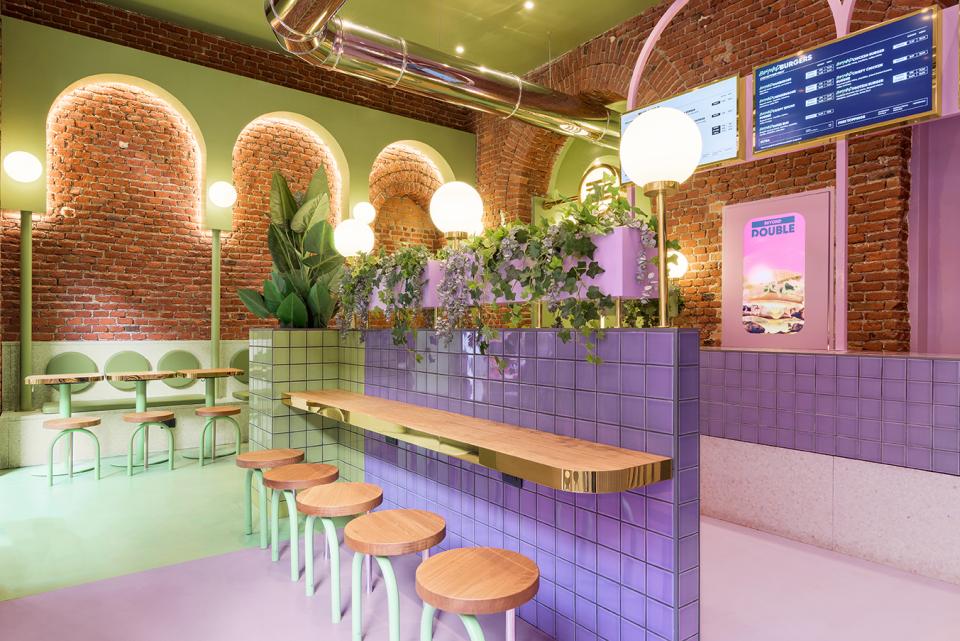 Vibrant interior design at Bun in Milan featuring pastel colors, greenery, and unique seating arrangements by Masquespacio.