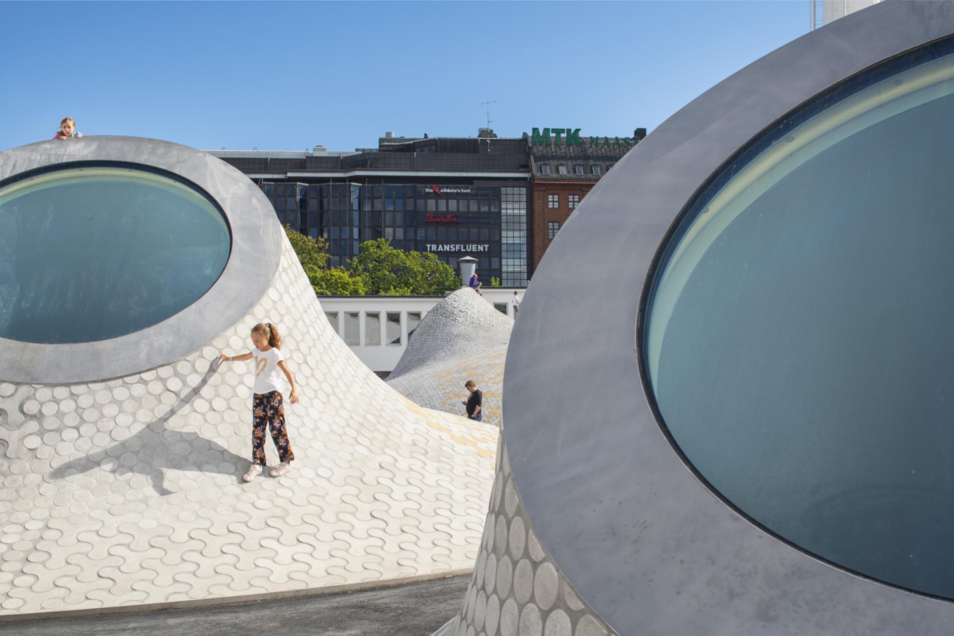Children play on the sculptural rooftop of Helsinki's new art museum, showcasing innovative architecture and design.