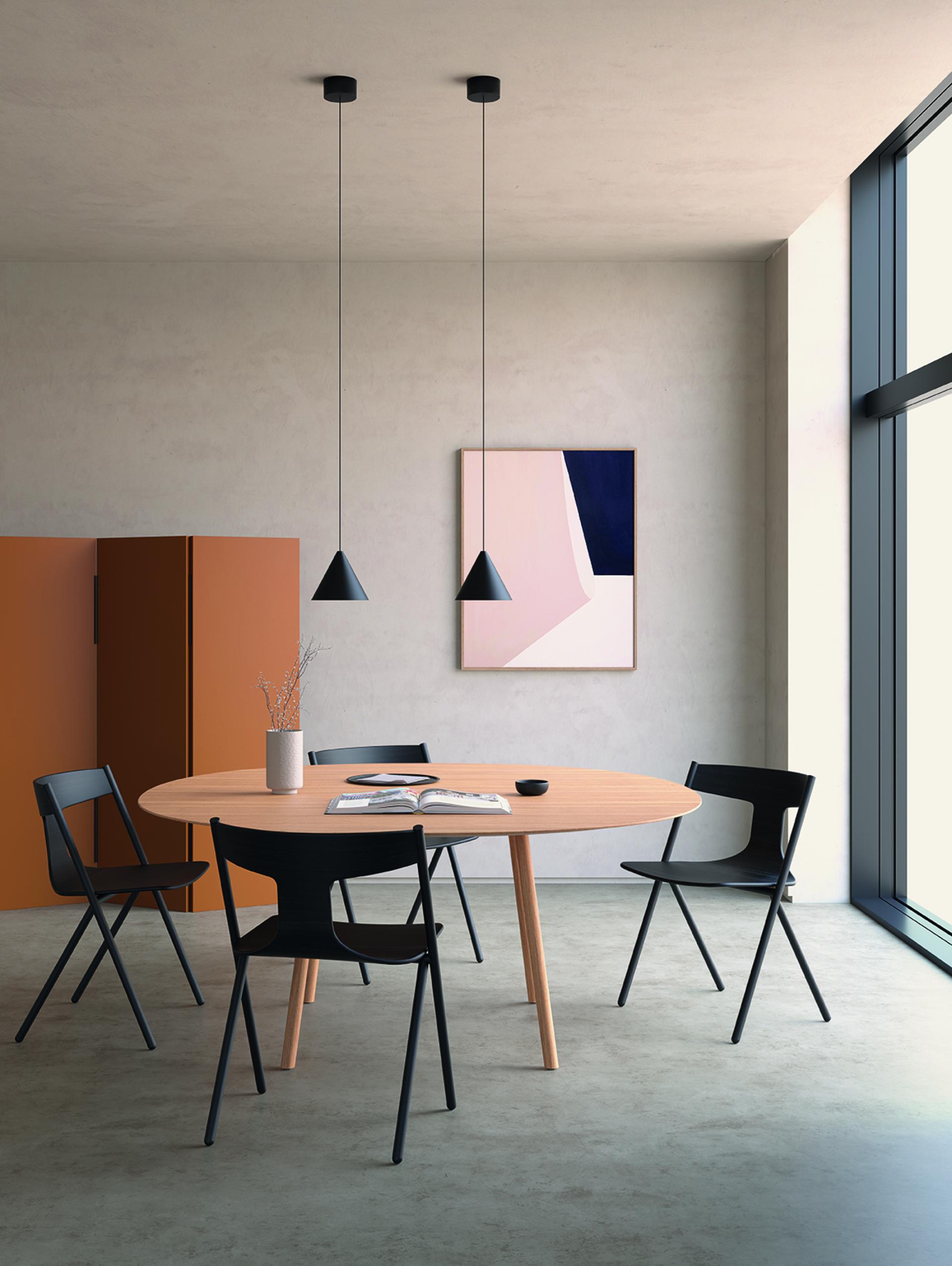 Modern dining area with a round wooden table, black chairs, and minimalist decor, highlighting Parisian design trends.