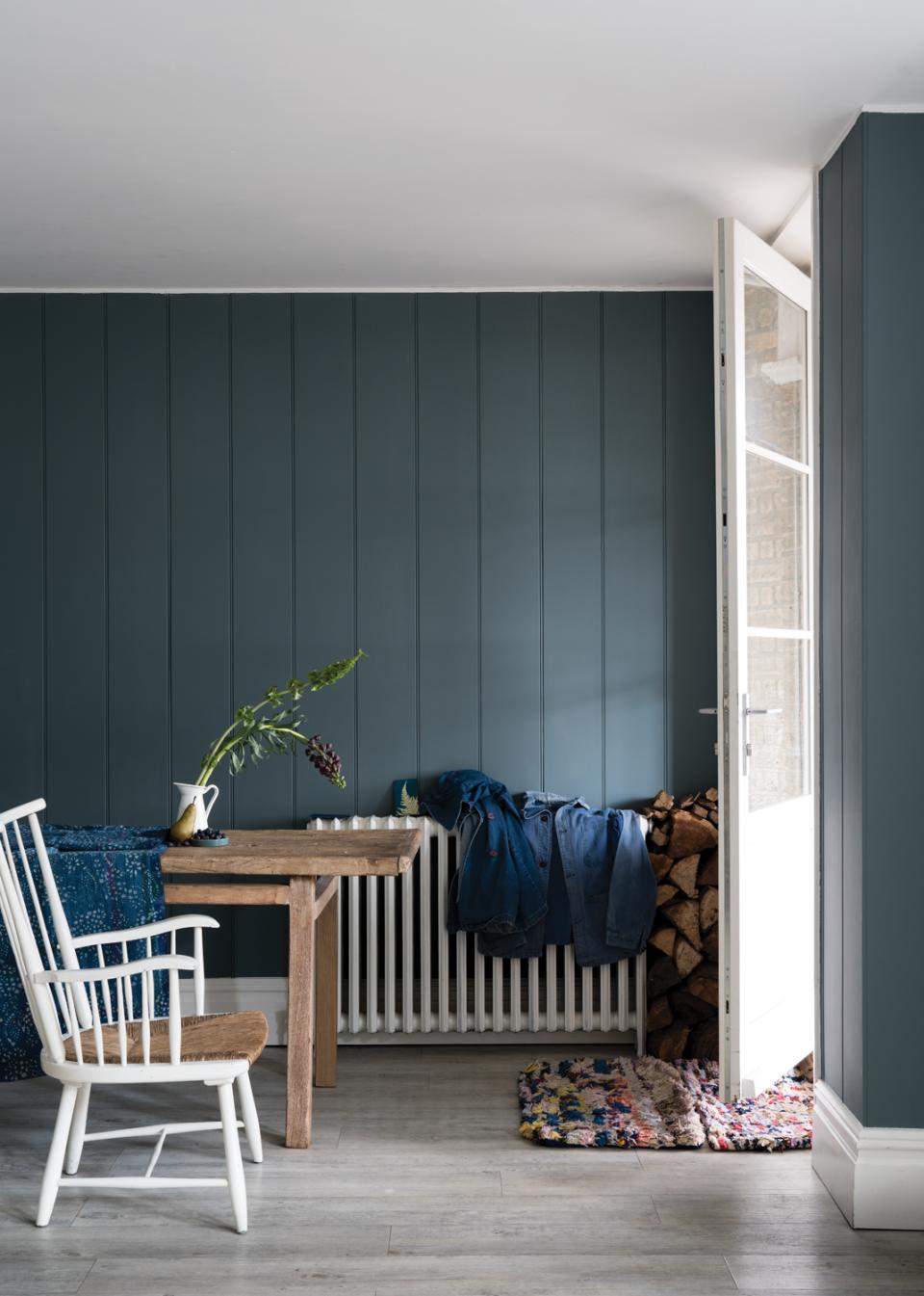 Cozy interior featuring a wooden table, white chair, and dark painted walls, showcasing Farrow & Ball's new paint colors.
