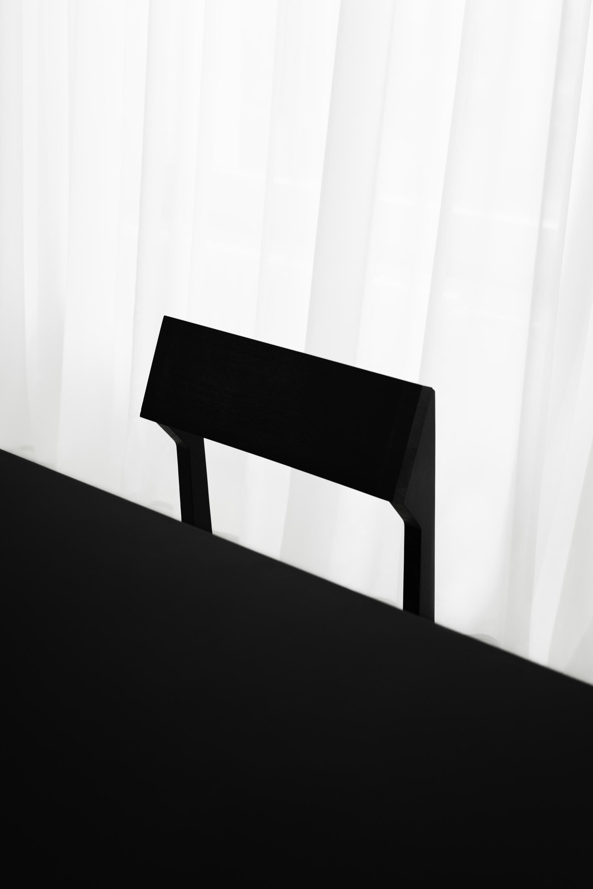 Minimalist black chair silhouette against a white curtain, showcasing contemporary interior design by Vaust Studio Berlin.
