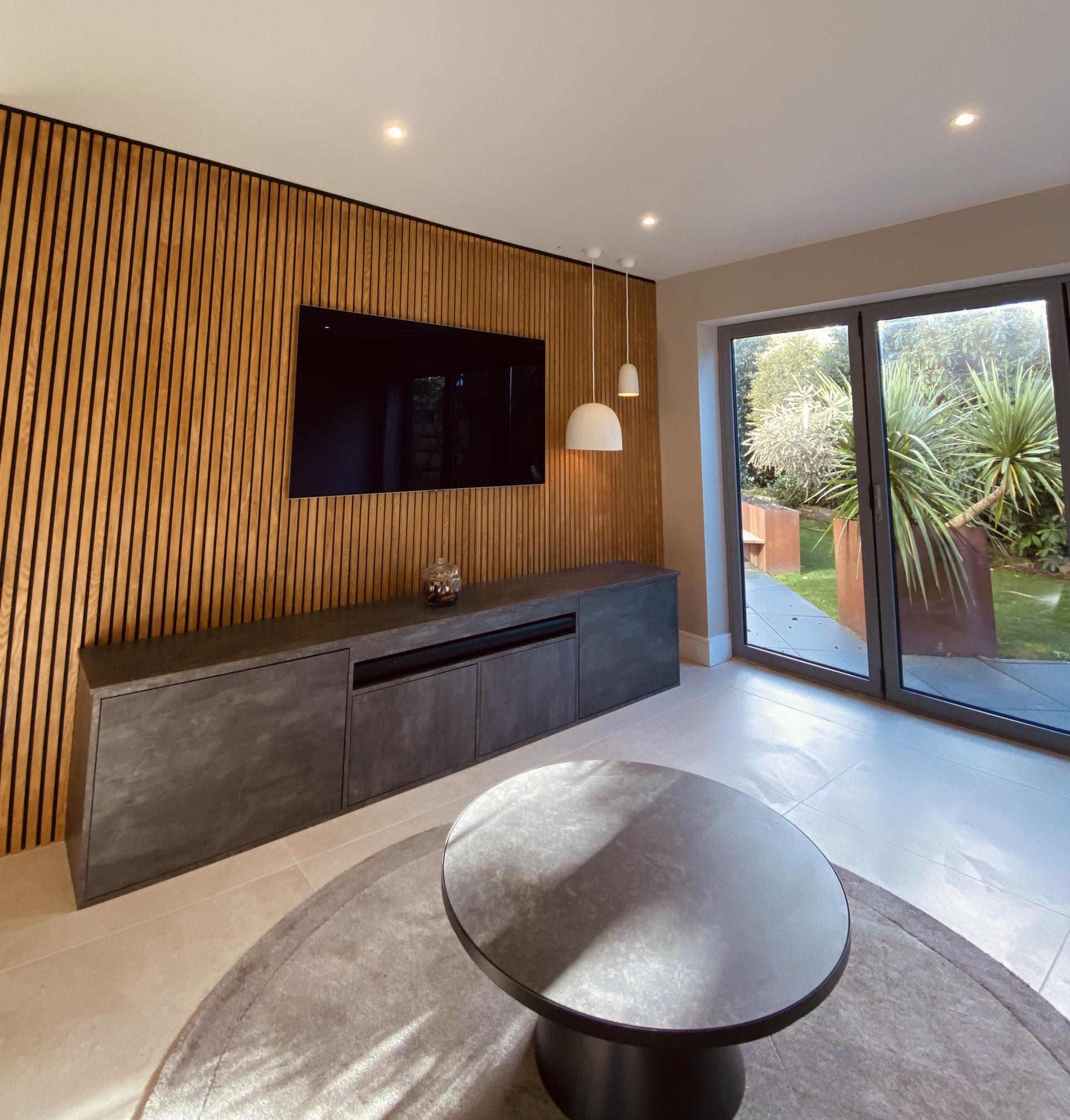 Modern living room design featuring sleek furniture, wooden accent wall, and large glass doors leading to a garden.