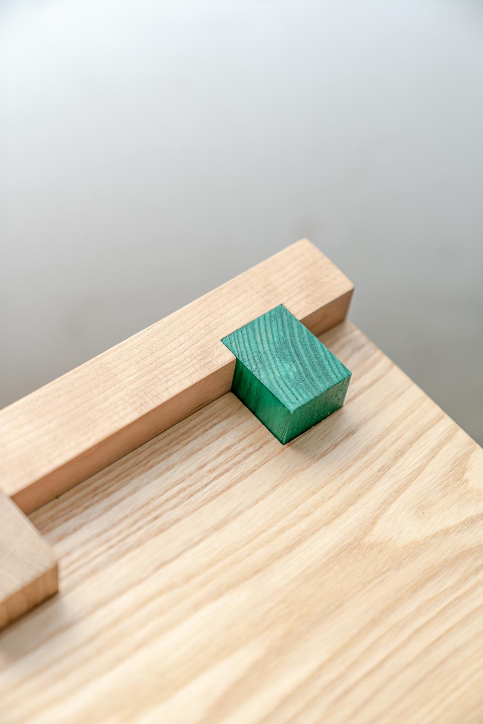 Crafted wooden mini-stool with a green block accent on a smooth light surface, showcasing minimalist design and craftsmanship.