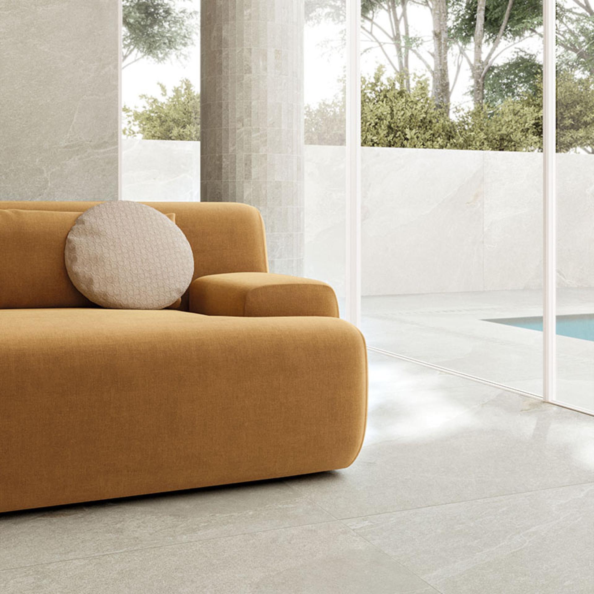 Modern yellow sofa with a decorative pillow, set against sleek stone flooring and large glass windows in a contemporary interior.
