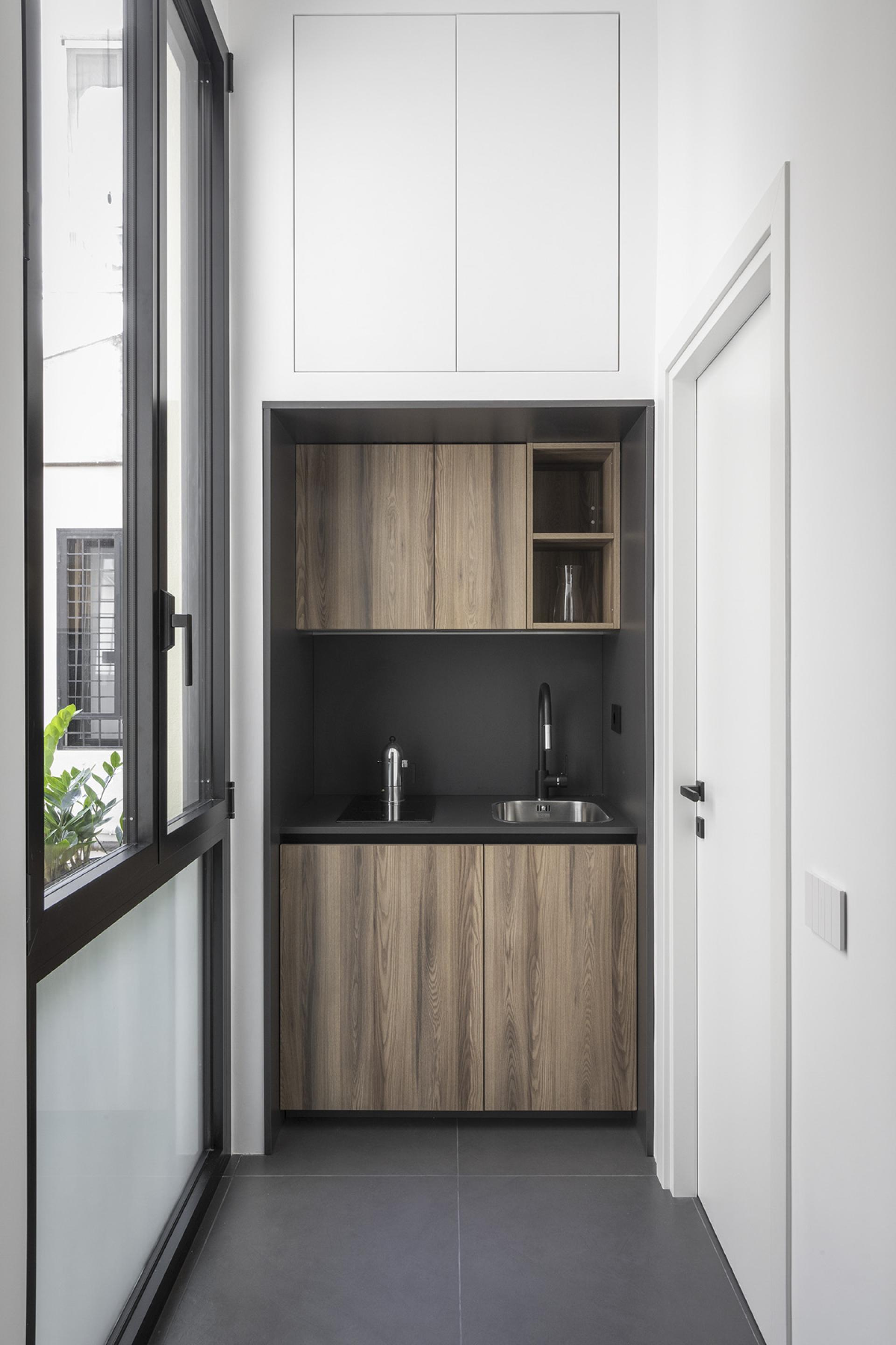 Compact modern kitchenette featuring wooden cabinetry, sleek black counter, and large windows overlooking greenery in Trastevere, Rome.