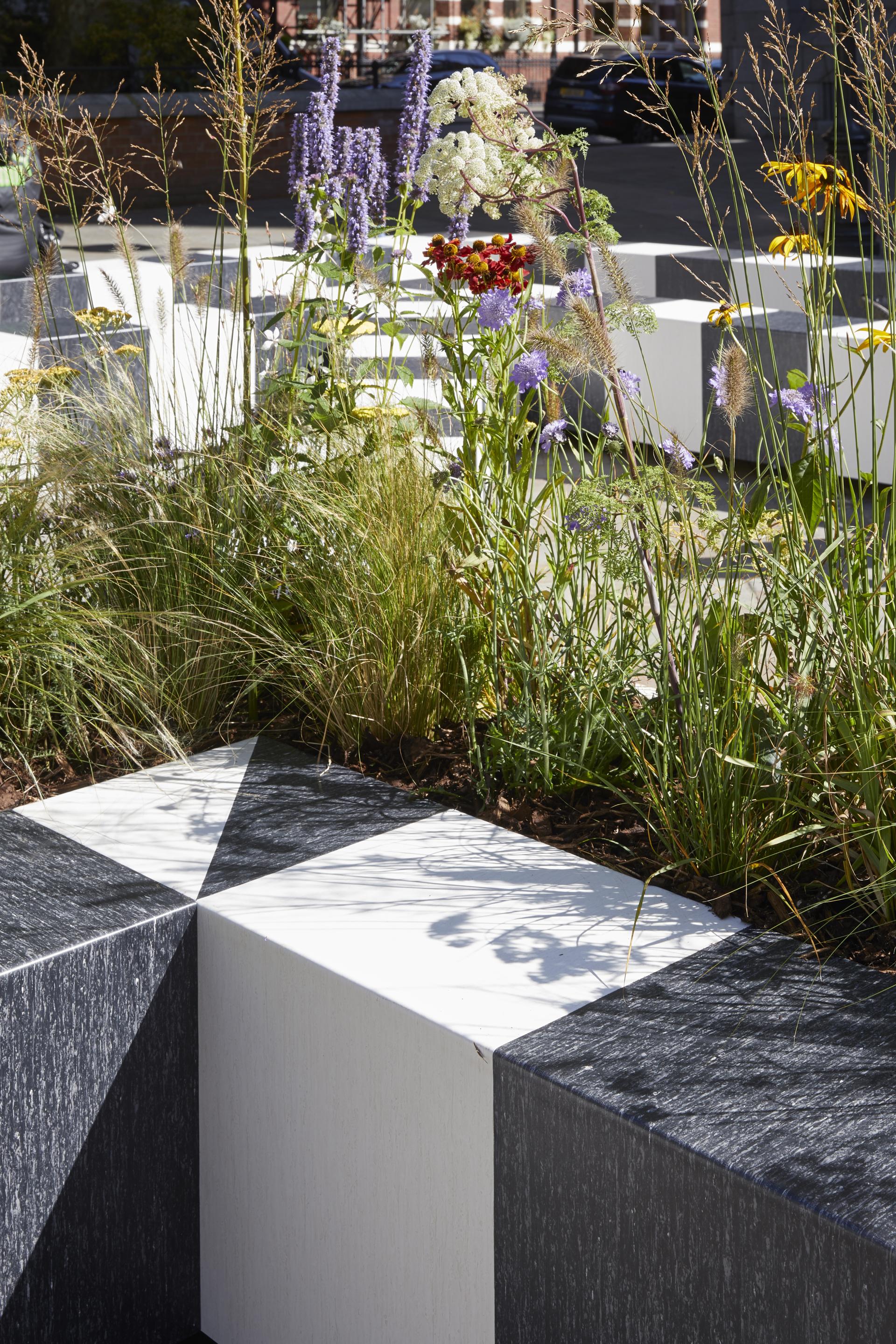 Textured black and white stone seating with vibrant flowers and greenery, creating a tranquil space at the London Design Festival.