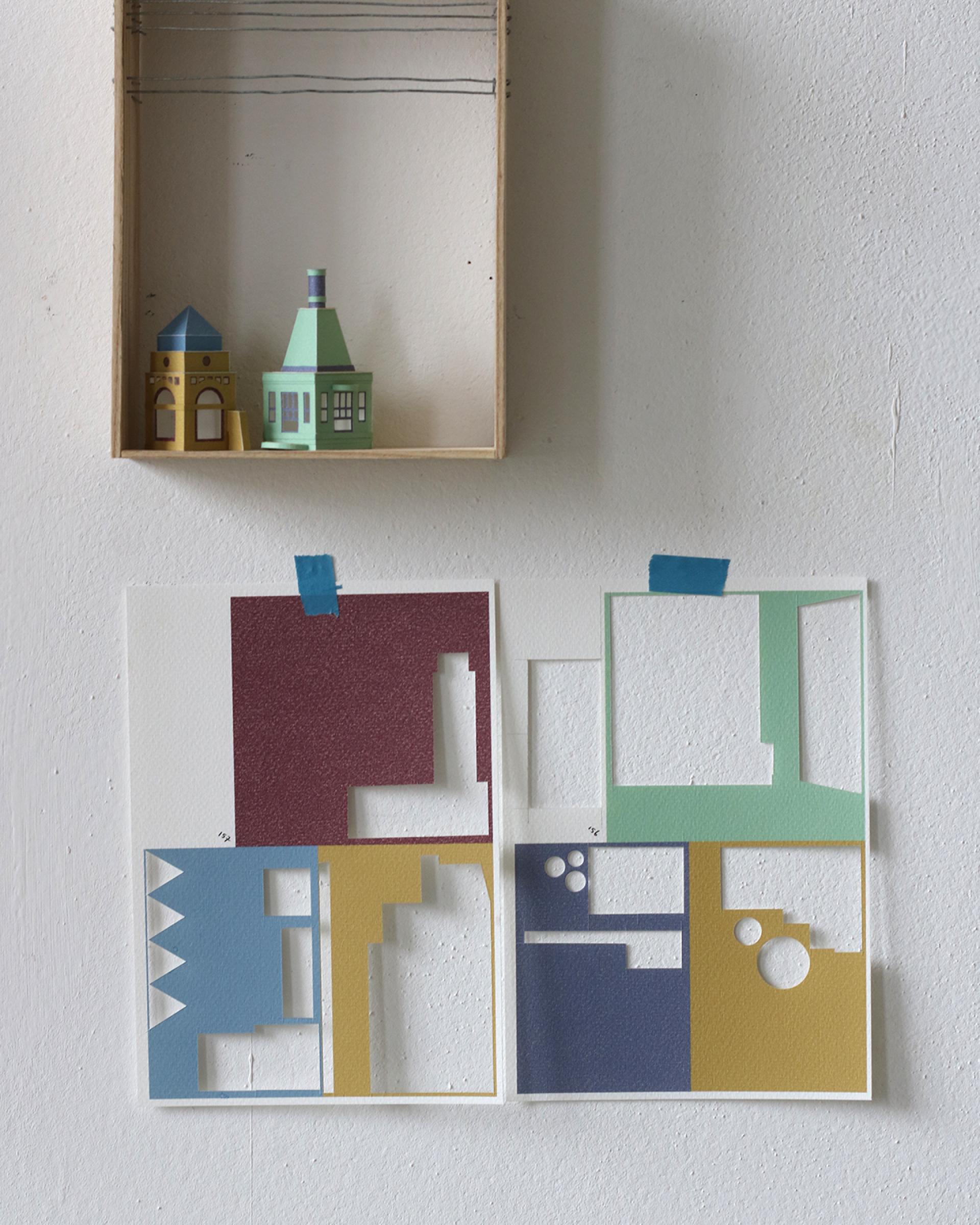 Colorful miniature paper buildings are displayed above cut-out paper patterns for model making, showcasing Charles Young's artistic process.