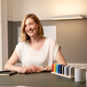 Hazel Pearson, director at Michael Laird Architects, smiles at a workspace table adorned with design materials and stationery.