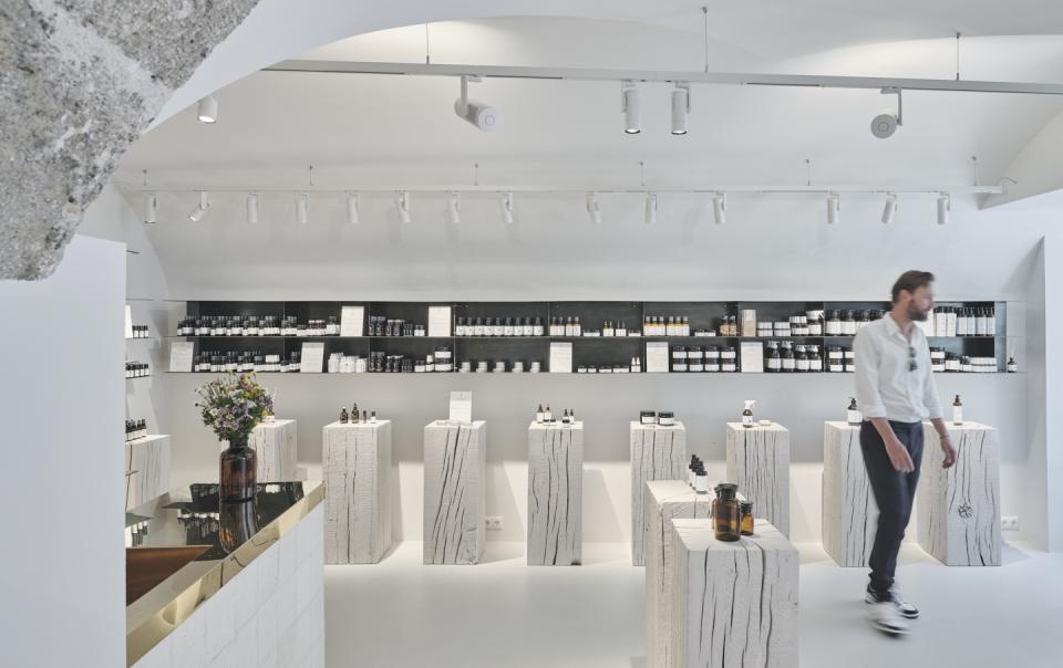 Bright, modern interior of Saint Charles store featuring natural cosmetics, wooden display stands, and a customer browsing products.