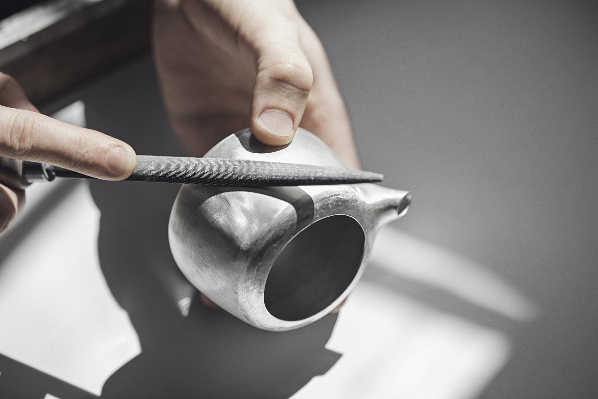 Artisan hands meticulously refining a metallic teapot, highlighting craftsmanship at London Craft Week 2019.
