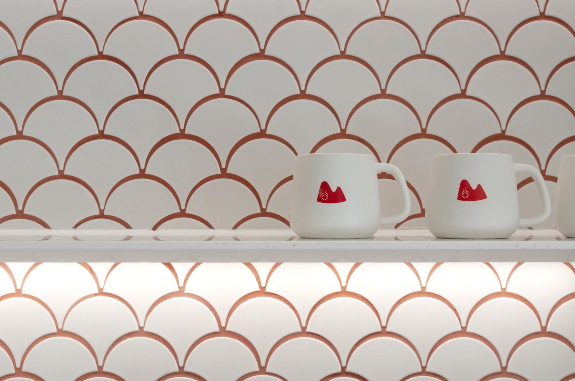Contemporary white mugs with red mountain designs displayed against a geometric scalloped tile backdrop at Unicorn Stores HQ.