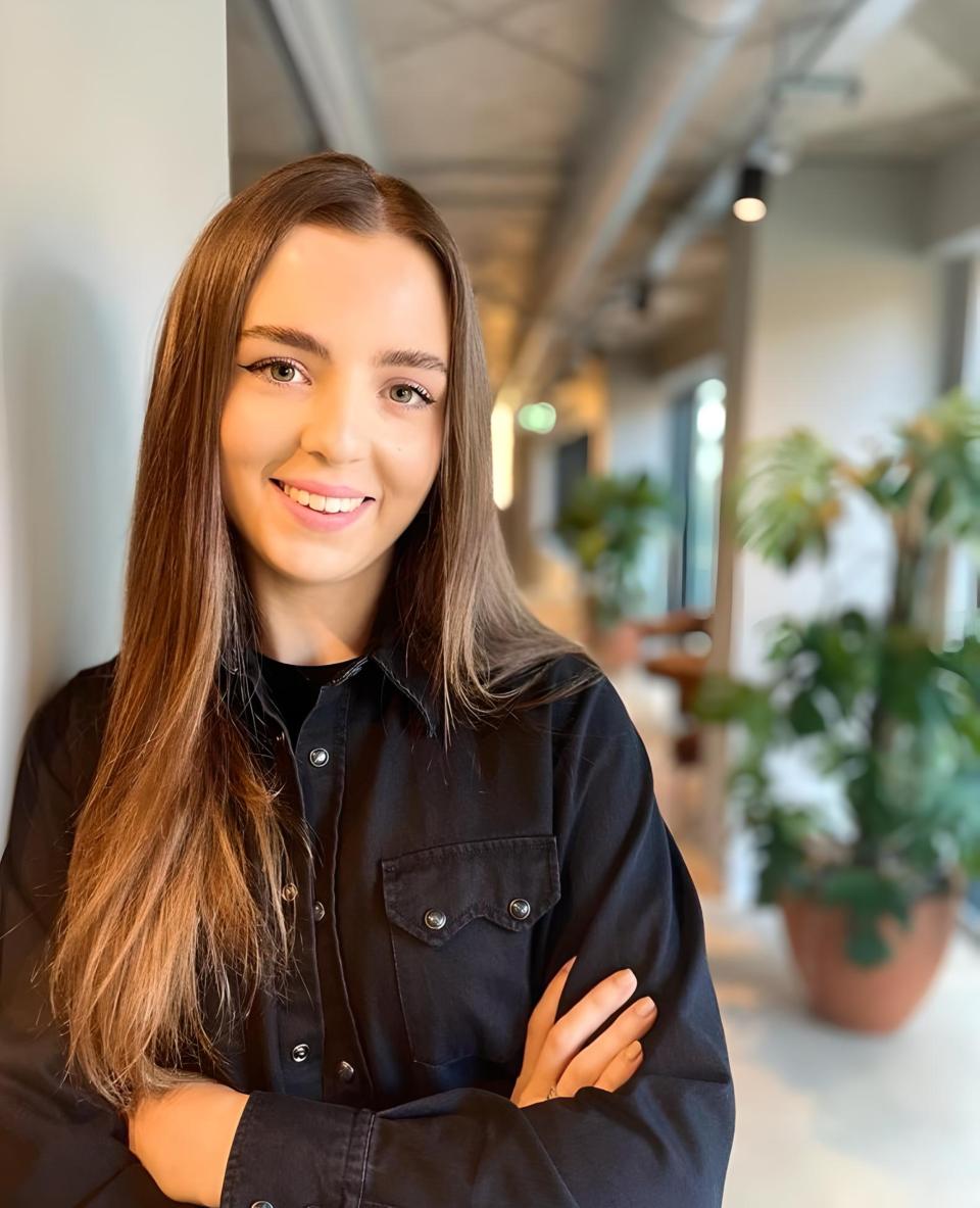 Courteney Kiely, founder of Scene Interiors, smiles confidently in a modern interior design studio surrounded by greenery.