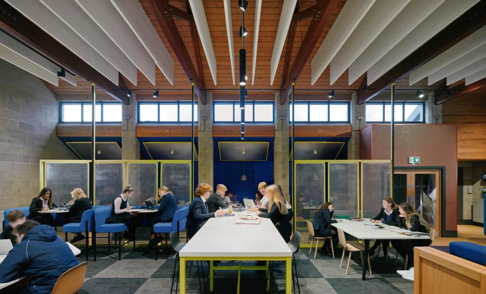 Modern study space in Sedbergh School's Queens Hall, featuring vibrant furniture, wooden beams, and students collaborating.