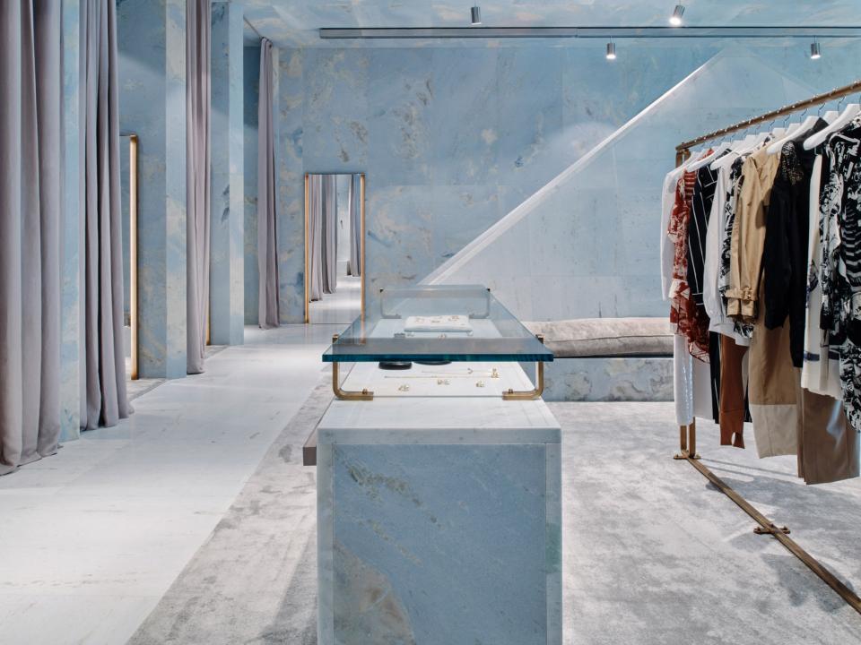 Céline's Miami store interior features blue marble walls, elegant clothing displays, and luxurious, minimalist design elements.