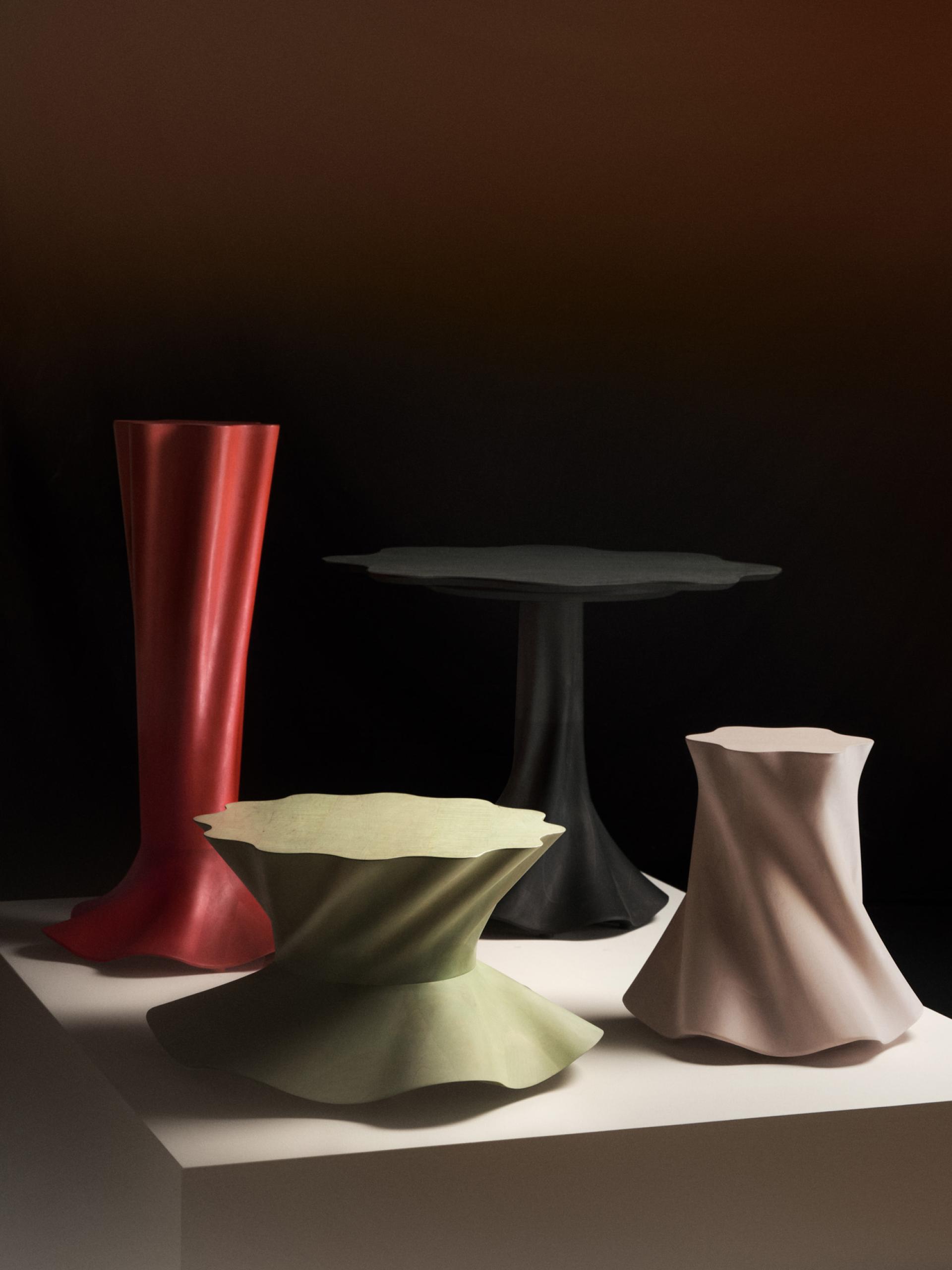 Colorful, sculptural furniture pieces including a red lipped vase and various textured stools on a display surface.