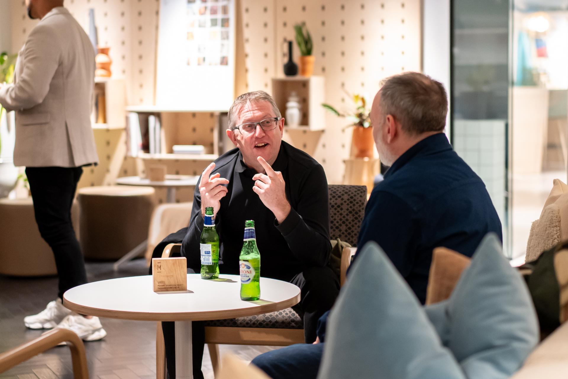 Two men engaged in a discussion over drinks in a modern, stylish interior, reflecting EDI culture and collaboration.