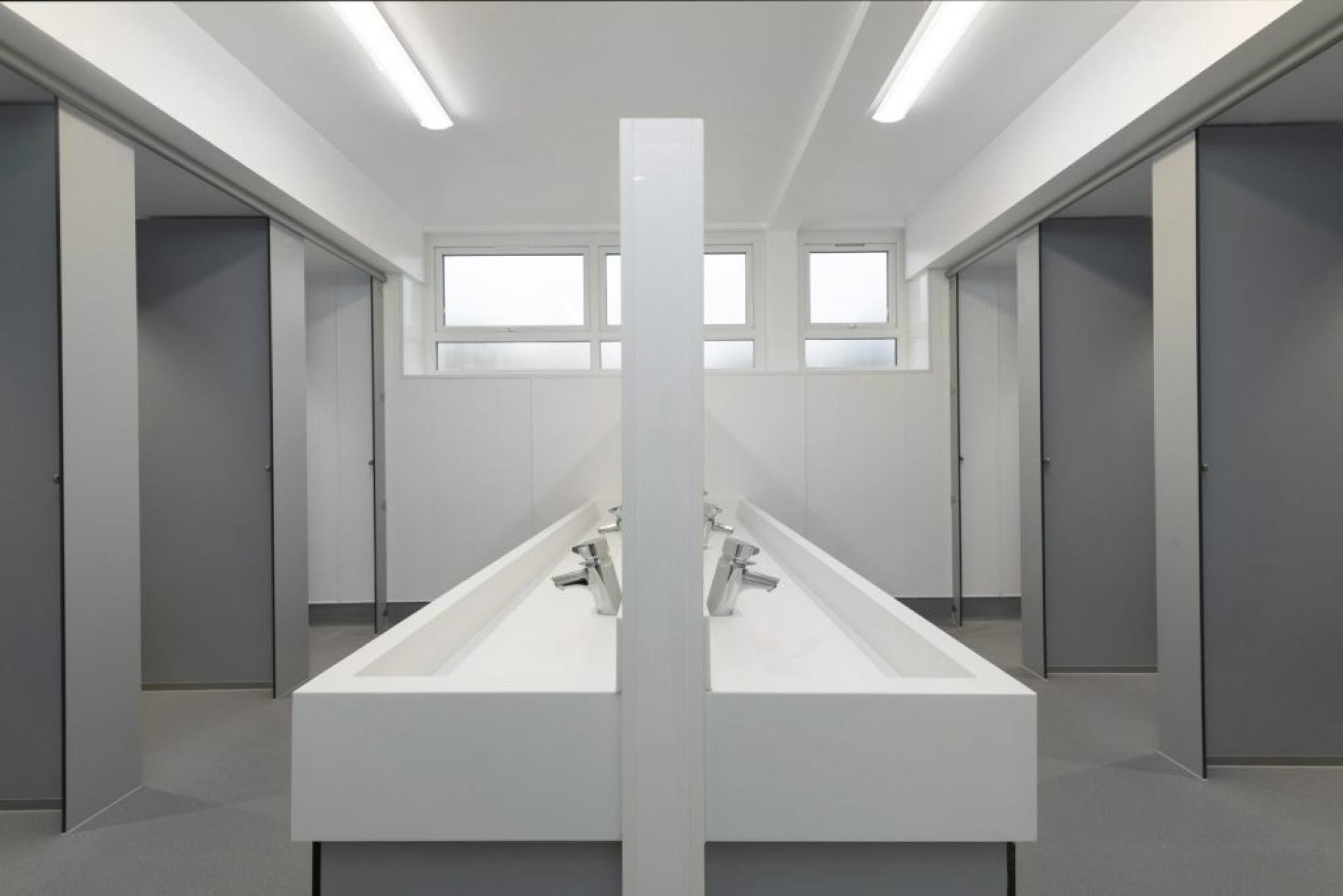 Modern restroom with multiple sinks and grey partition doors, showcasing thoughtful design by Material Source Studio Glasgow.