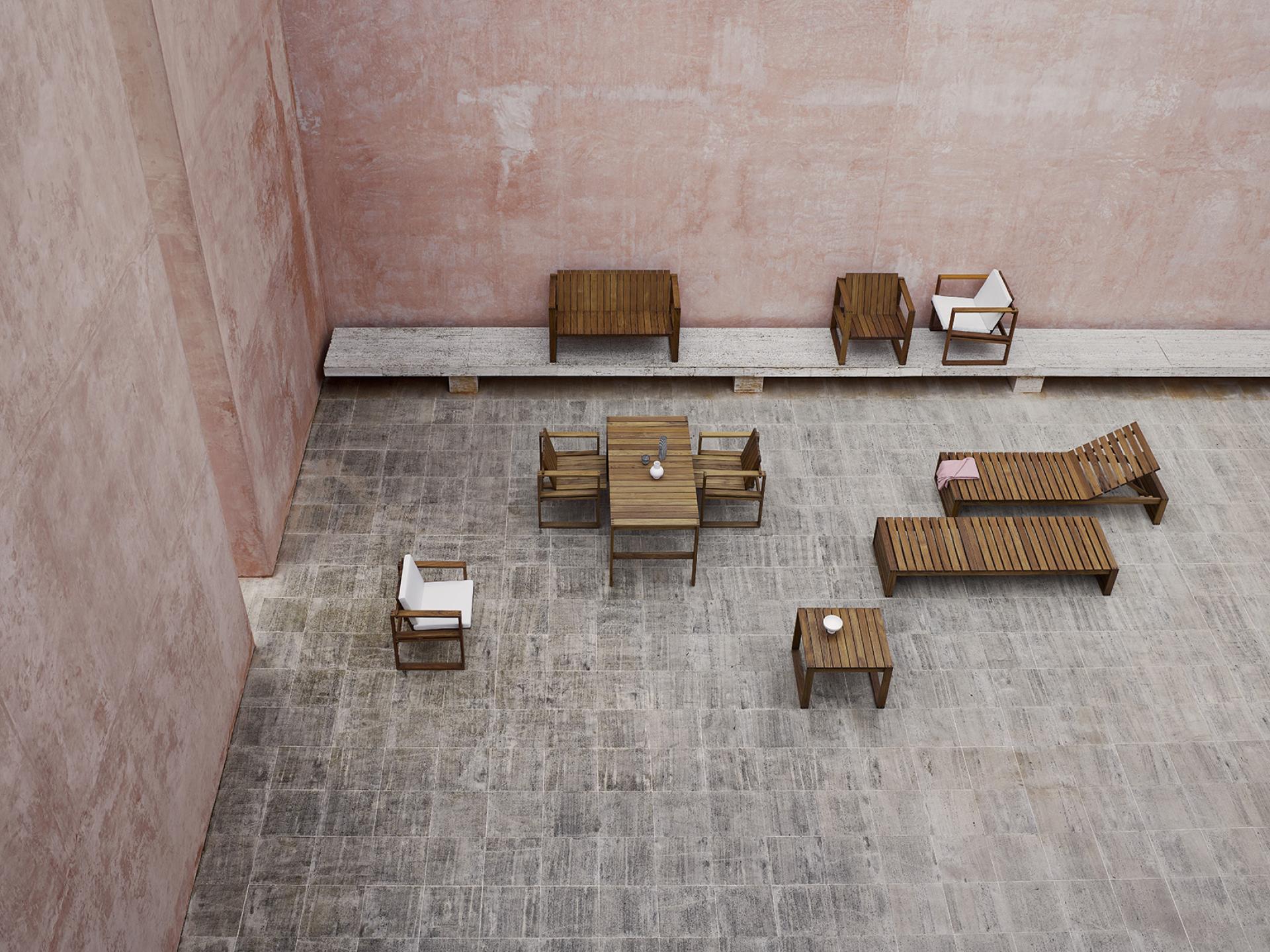 Elegant wooden outdoor furniture arranged on a stone patio, featuring chairs, tables, and loungers in a spacious setting.