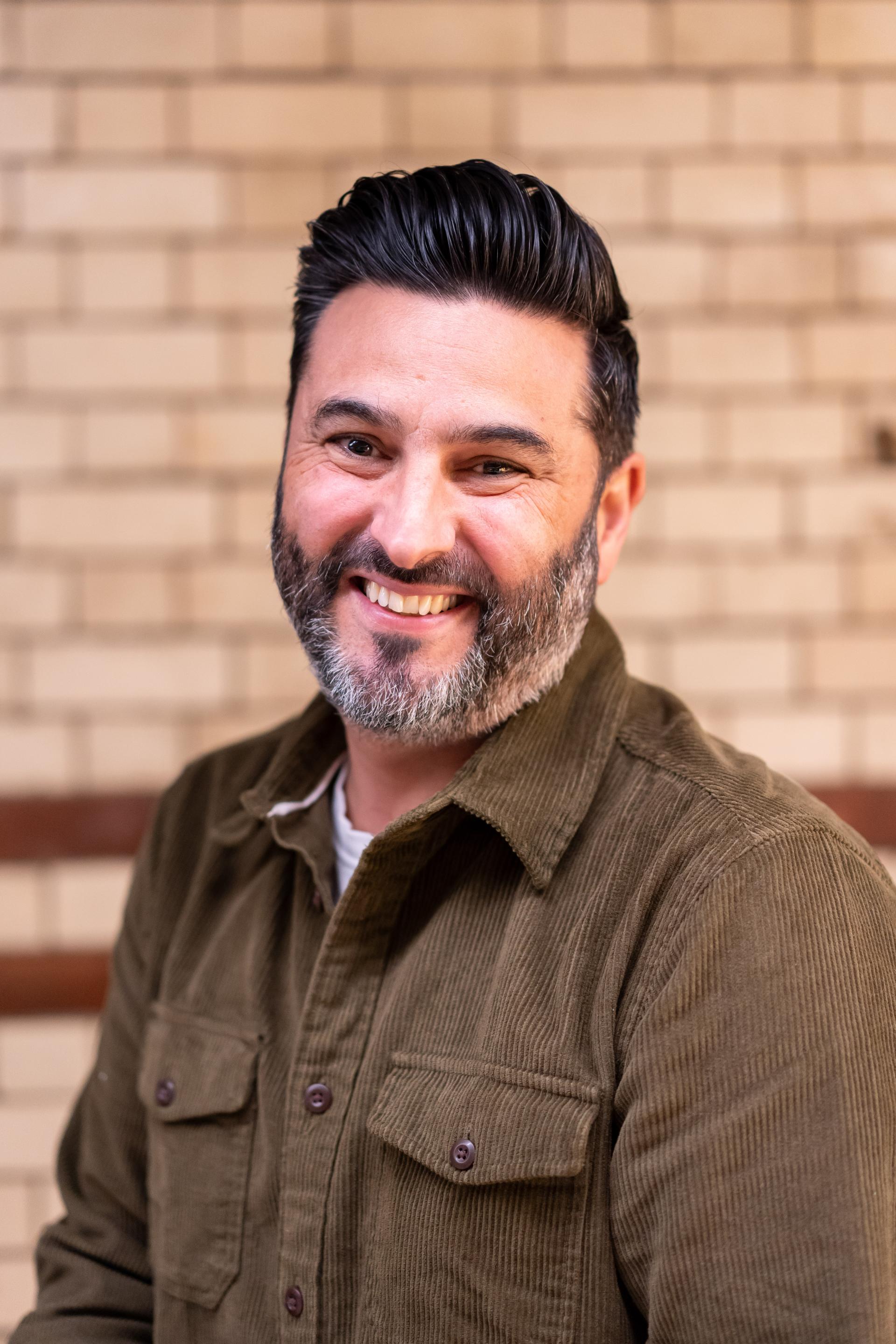 Smiling man in a corduroy shirt, discussing EDI culture in an inviting studio setting.