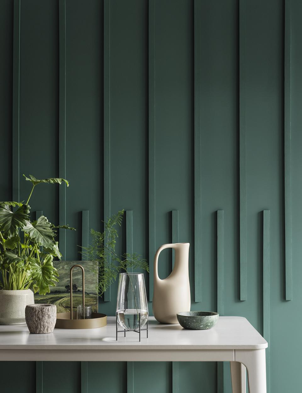 Stylish tabletop arrangement featuring greenery, modern ceramics, and a textured teal wall, highlighting SS22 color trends from Crown Paints.