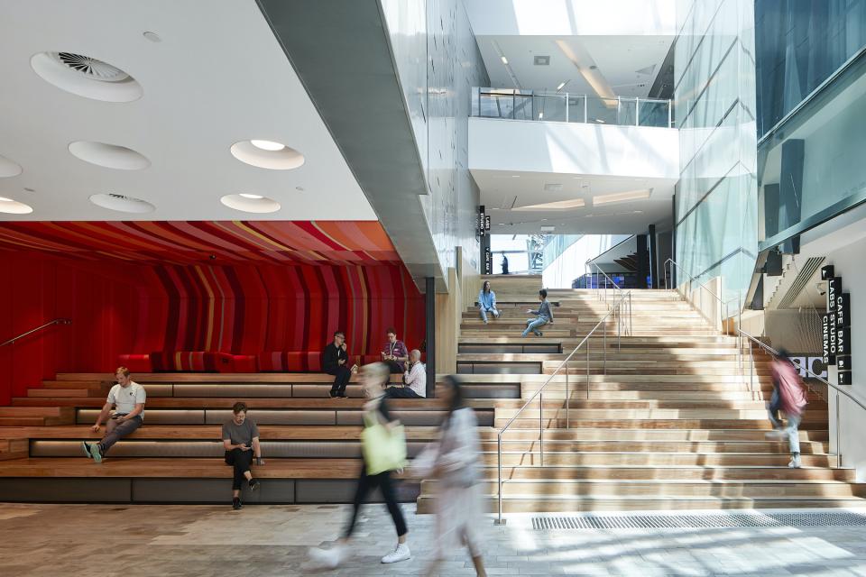 Modern interior of ACMI in Melbourne featuring vibrant seating areas and an expansive staircase with visitors.