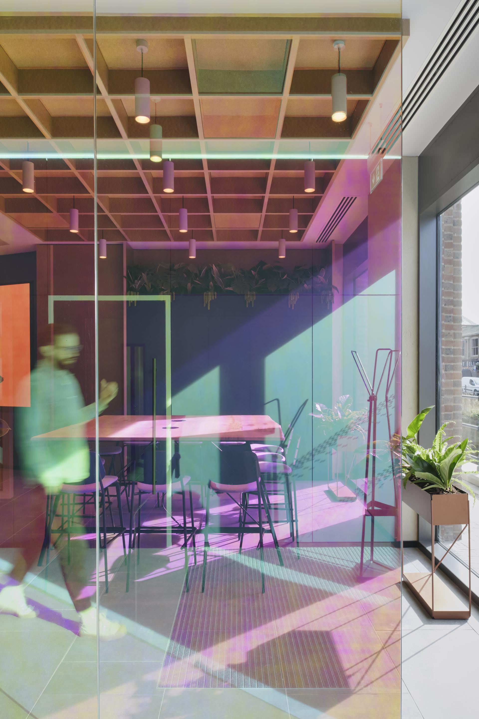 Modern office interior featuring colorful glass partitions, a wooden table, chairs, and lush greenery, reflecting Ekho Studio's design aesthetic.