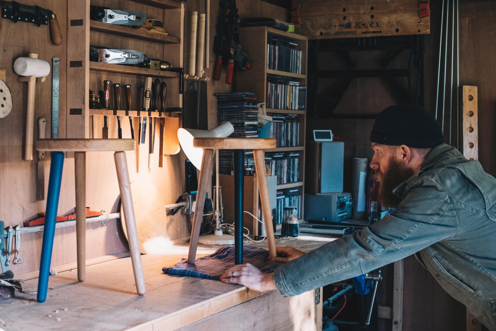 Craftsman adjusting colorful wooden stools in a workshop, showcasing local craftsmanship and furniture design.