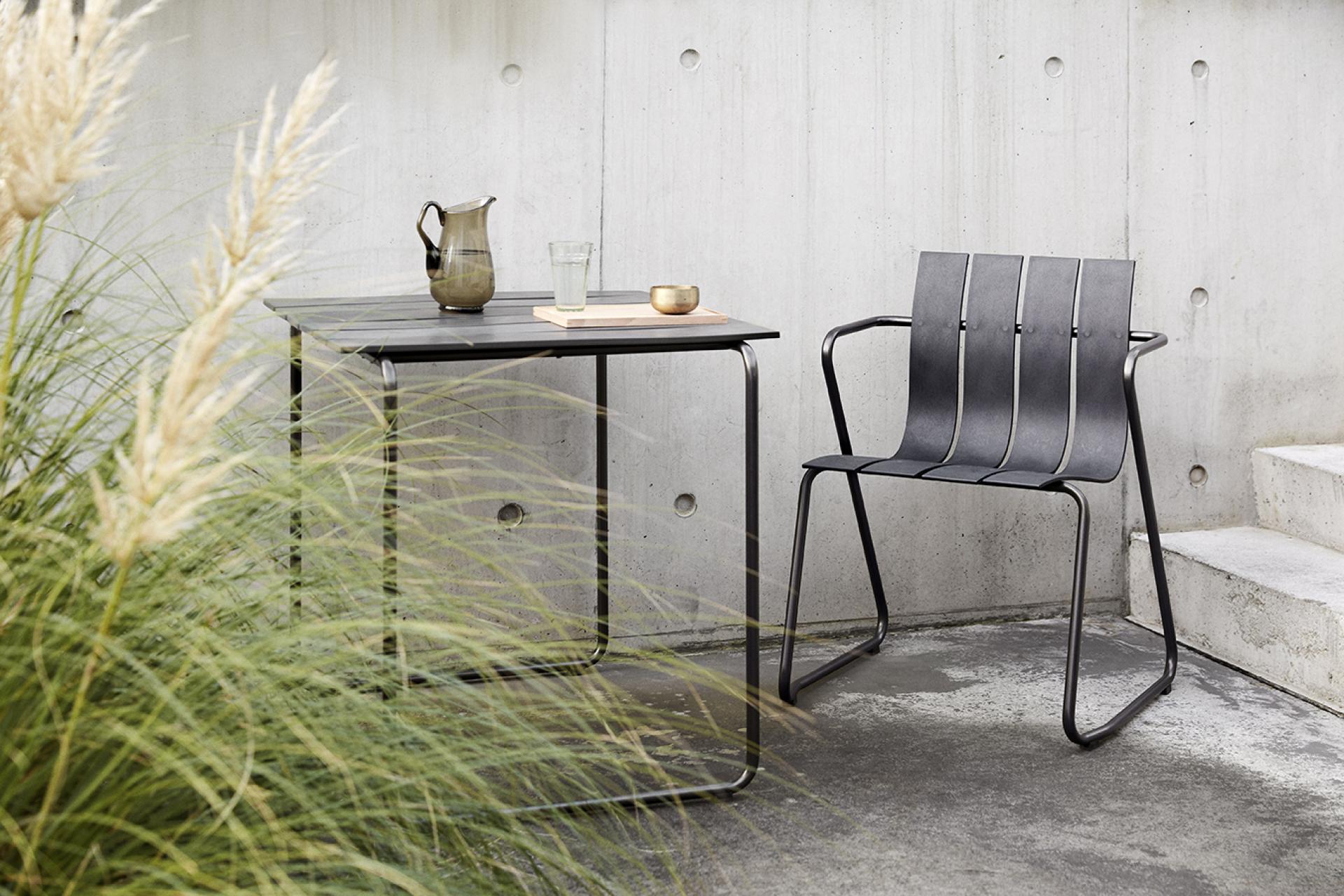 Stylish black metal chair and table from Mater's Ocean Collection, set against a minimalist concrete backdrop.