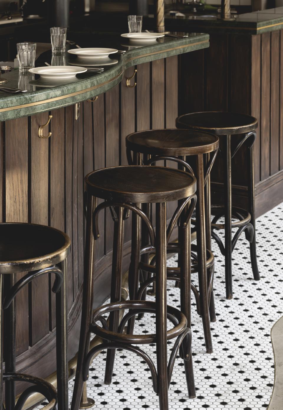 Stylish bar stools align with a polished green countertop in a Parisian-inspired wine bar interior design.