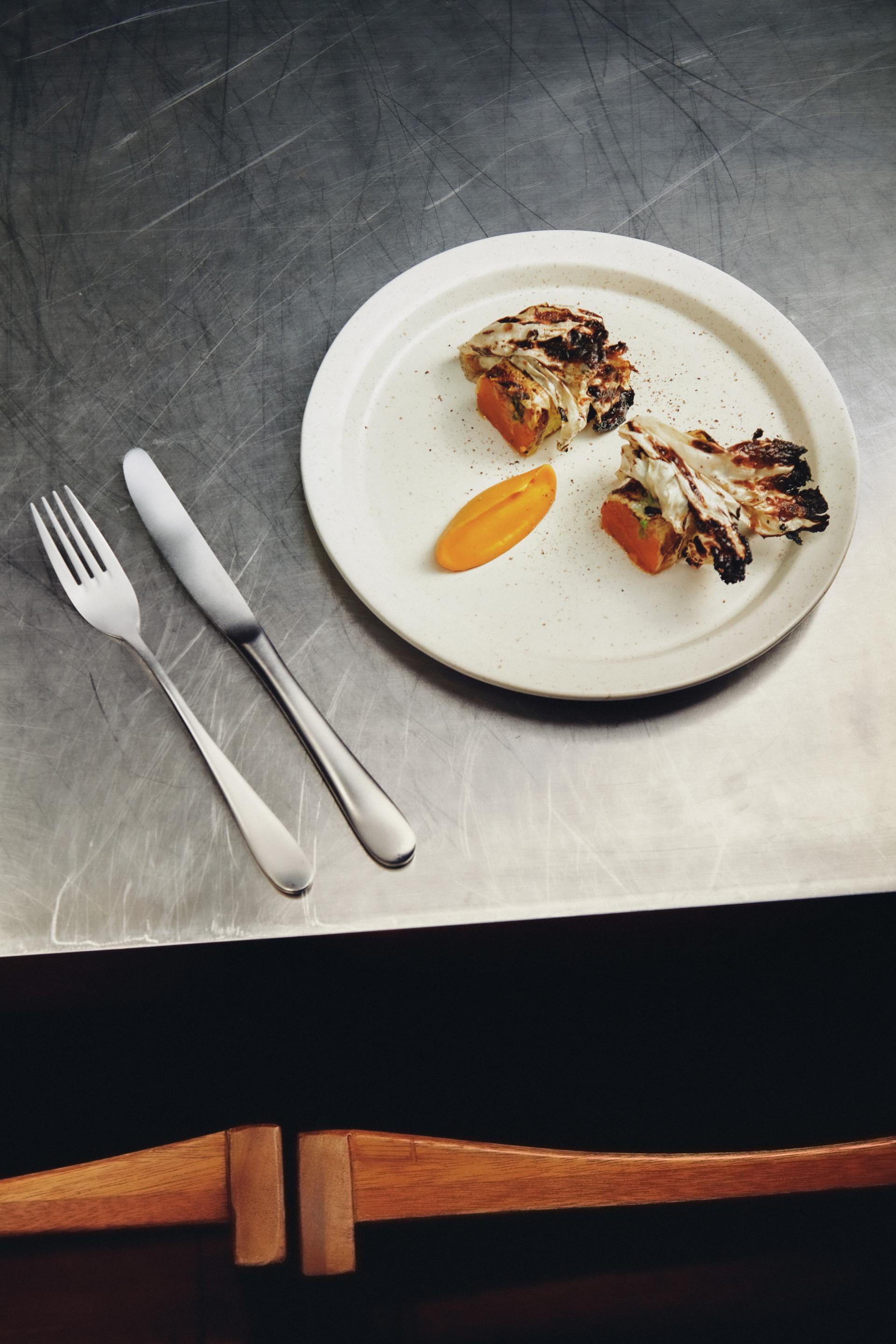 A beautifully plated dish featuring grilled vegetables and a vibrant sauce, set against a sleek metallic table.