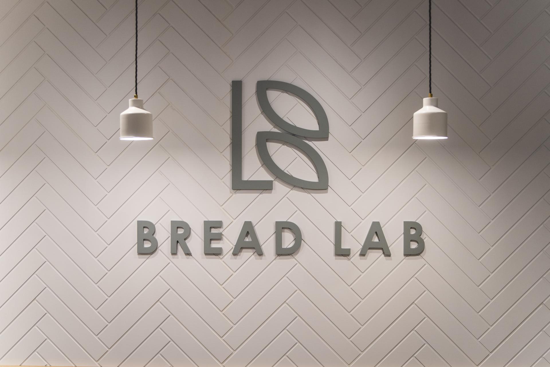 Stylish minimalist interior showcasing the Bread Lab logo on textured herringbone wall with hanging lights.