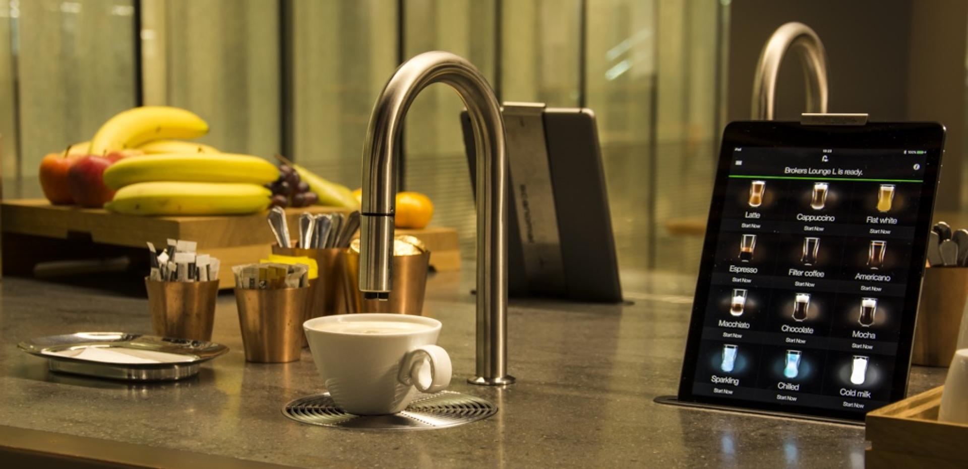 Modern coffee setup featuring Scanomat's TopBrewer, showcasing brewing options on a tablet and a coffee cup.