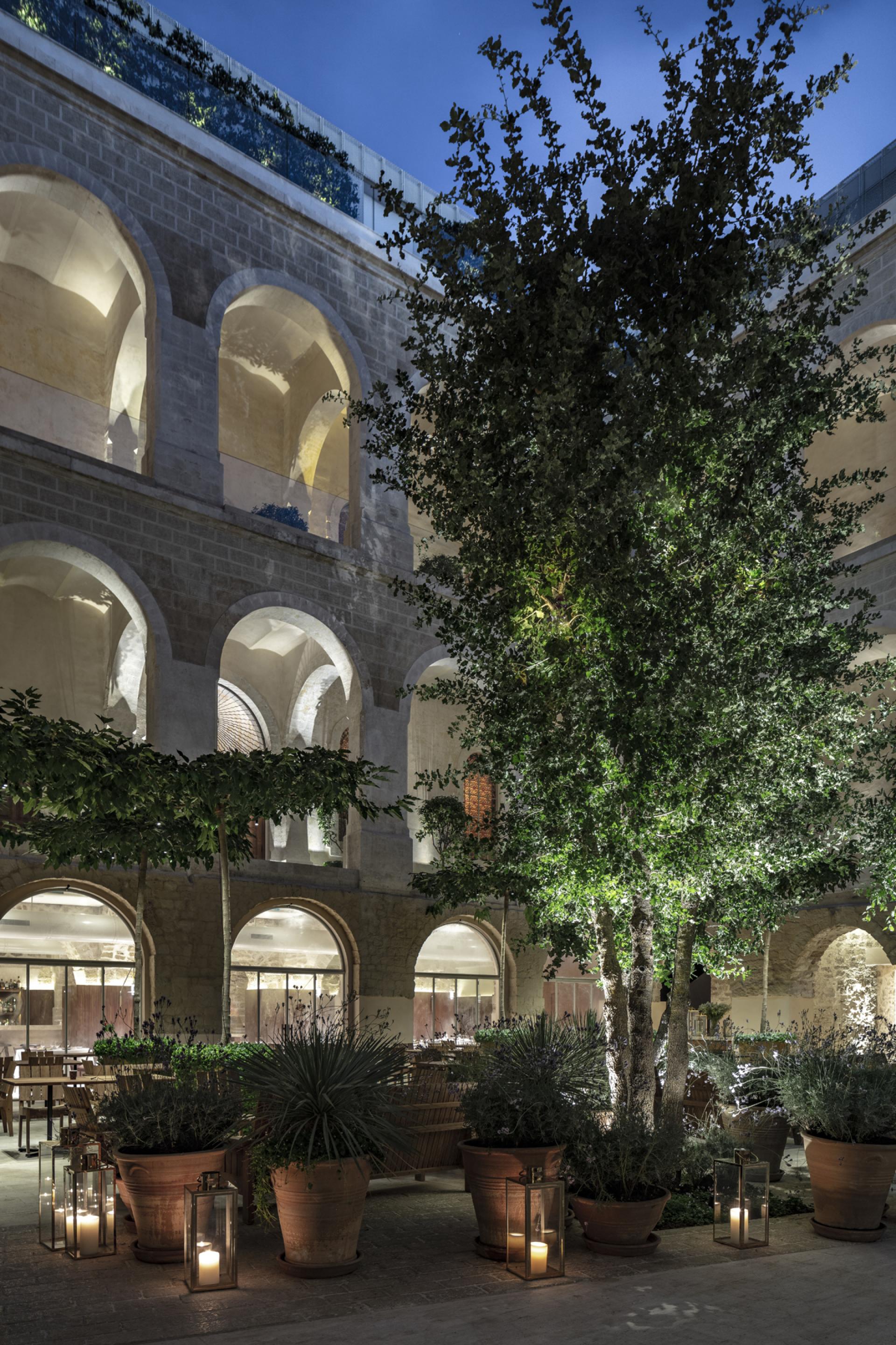 Minimalist courtyard at The Jaffa, featuring arched architecture, greenery, and ambient lighting, designed by John Pawson.