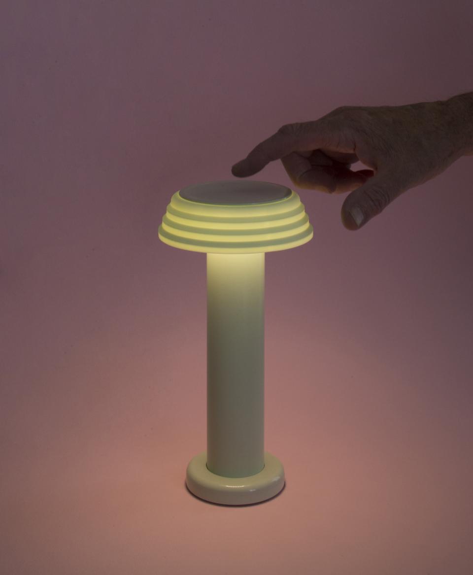 A hand adjusts the glow of a sleek, modern lamp from the SowdenLight SHADES collection against a pink backdrop.