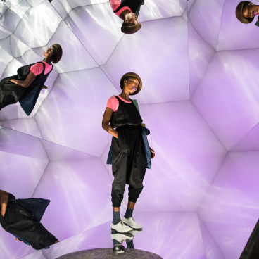 A model poses in a vibrant installation featuring mirrored surfaces and purple lighting at Clerkenwell Design Week.