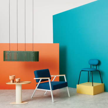 Modern furniture display featuring a blue armchair, pendant light, and colorful accent pieces at 100% Design event.