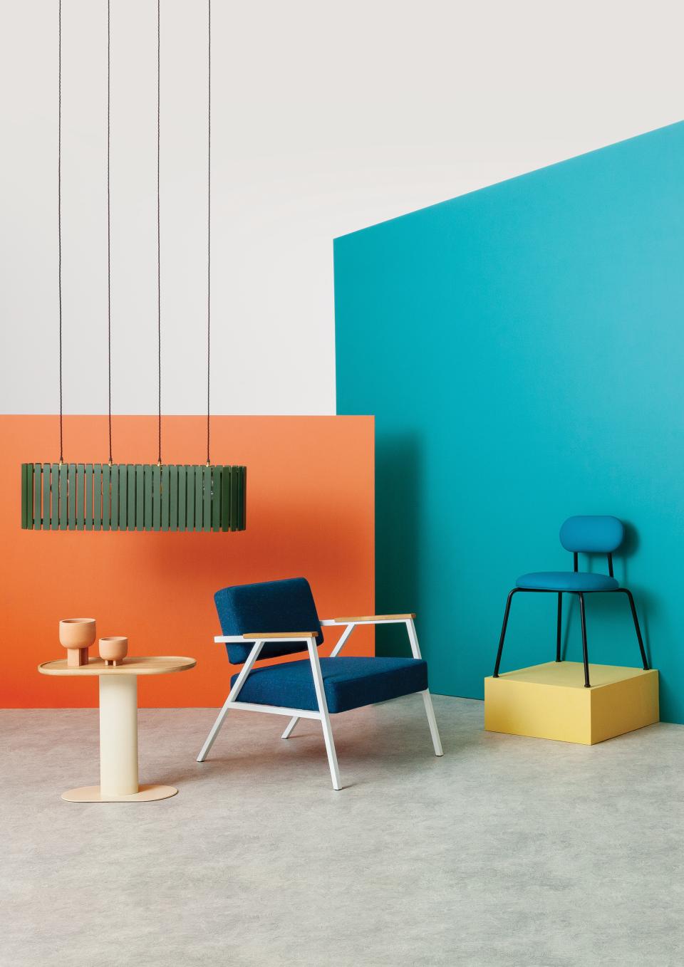 Modern furniture display featuring a blue armchair, pendant light, and colorful accent pieces at 100% Design event.