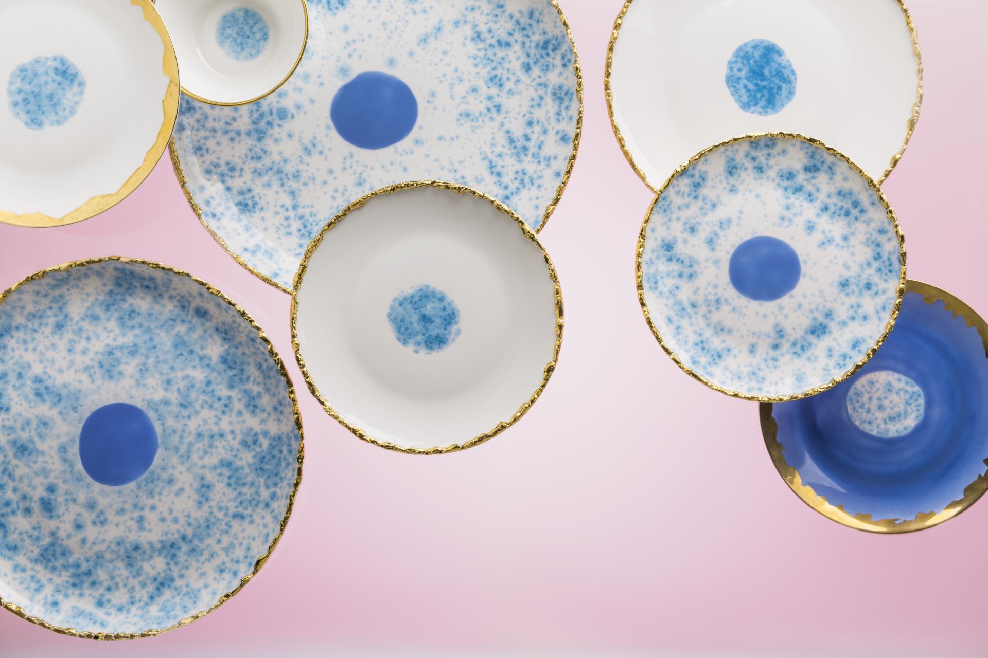 Colorful ceramic plates with blue patterns and gold edges, showcasing Coralla Maiuri's unique and experimental design style.