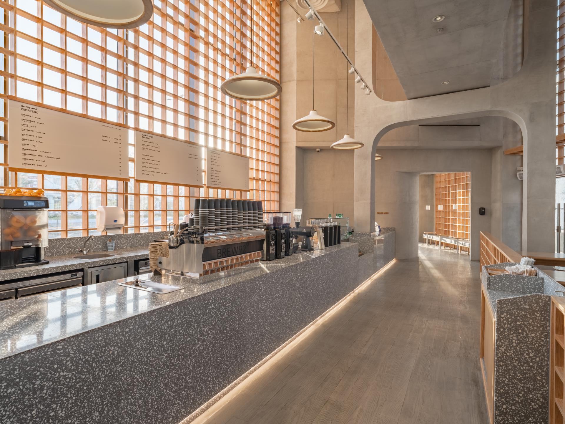 Modern coffee shop interior featuring a Japandi aesthetic with light wood, stone surfaces, and large windows.