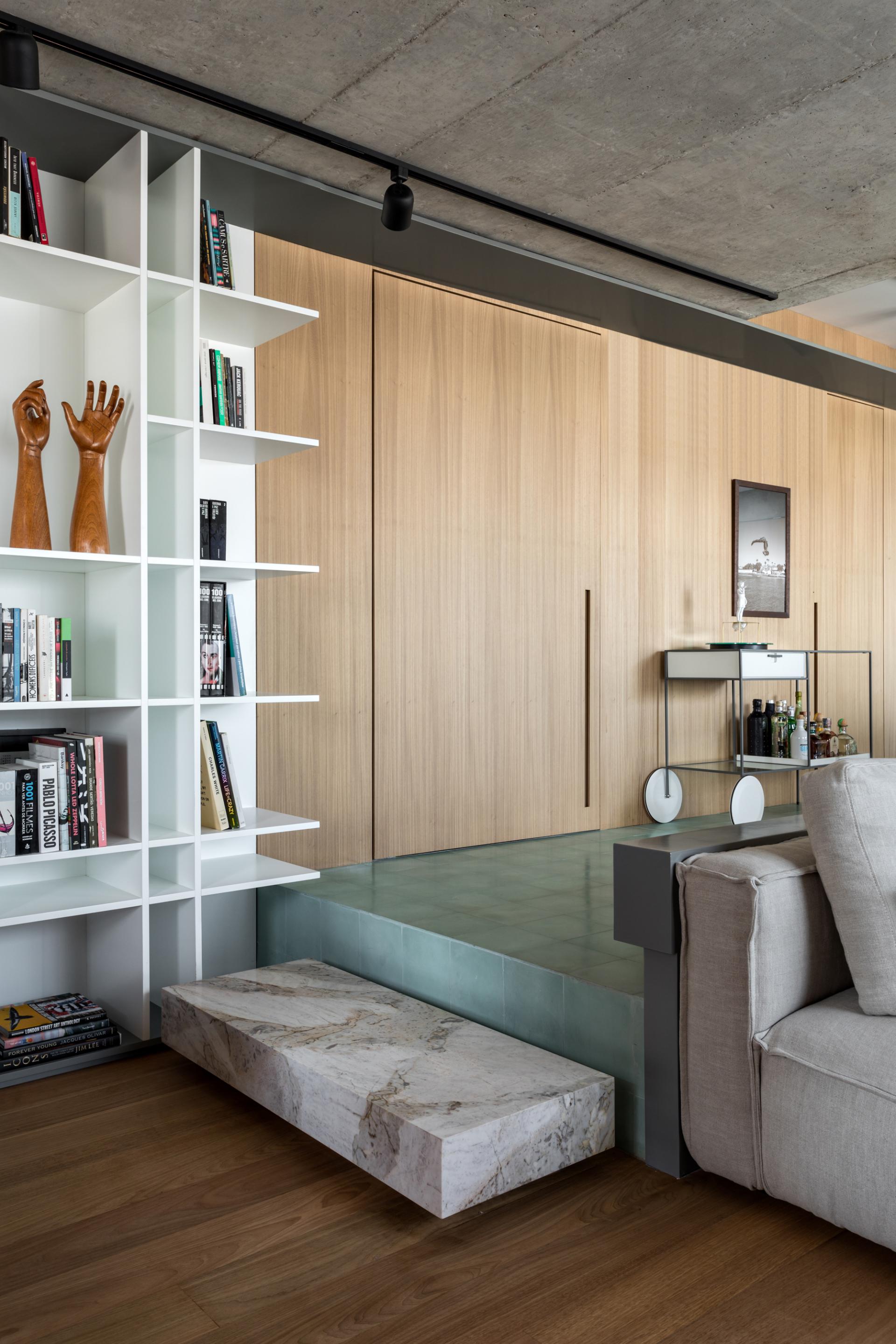 Stylish integrated apartment in São Paulo featuring a modern bookshelf, marble step, and elegant wooden wall design.