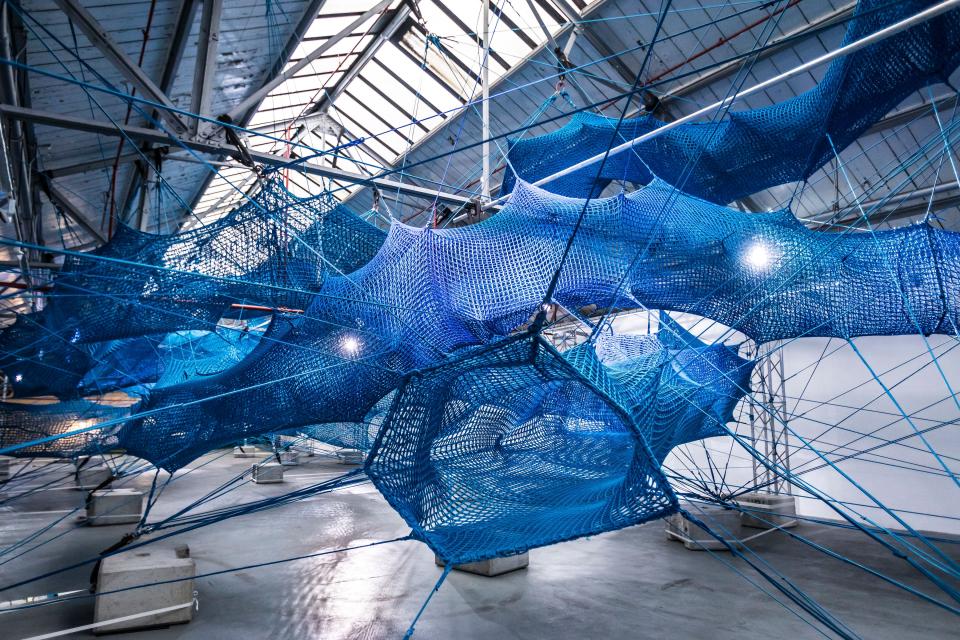 An immersive blue woven installation suspended in an art space, part of Anya Hindmarch's Weave Project at London Fashion Week.