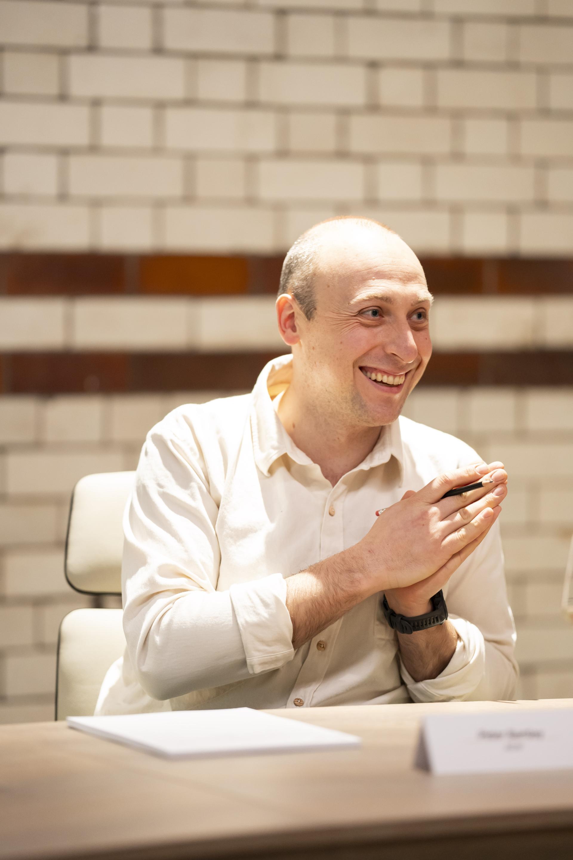 Man in a white shirt smiles and gestures while discussing technology's role in sustainability during a design meeting.