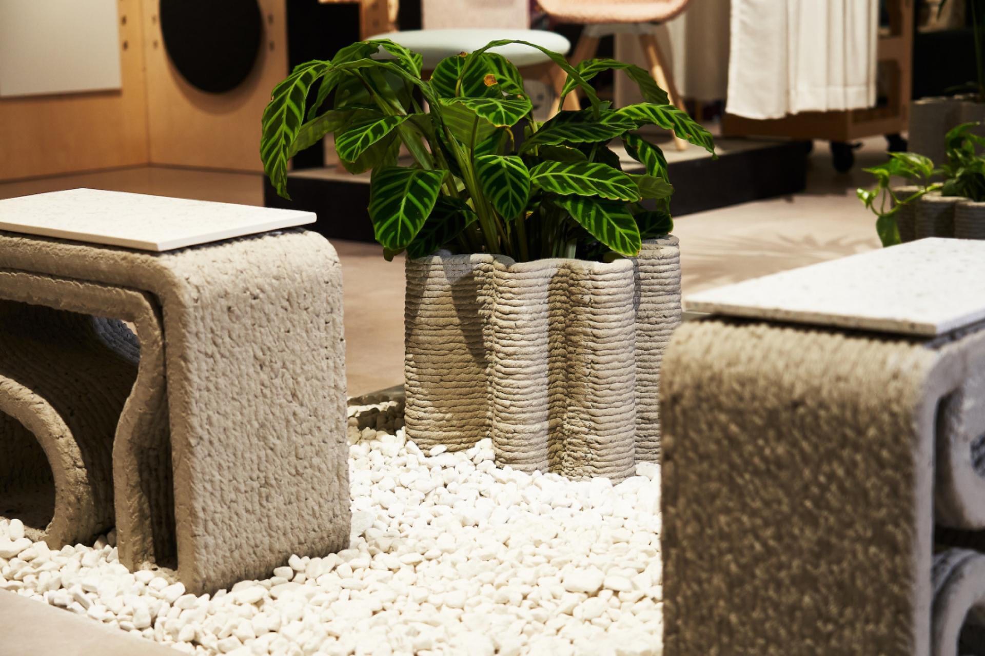 Modern 3D printed concrete planters and tables enhance sustainable design in an indoor exhibition space.