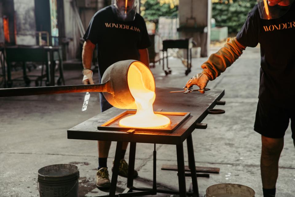 Workers pouring molten glass into a mold, showcasing the artistry of WonderGlass and nendo’s Melt furniture collection.