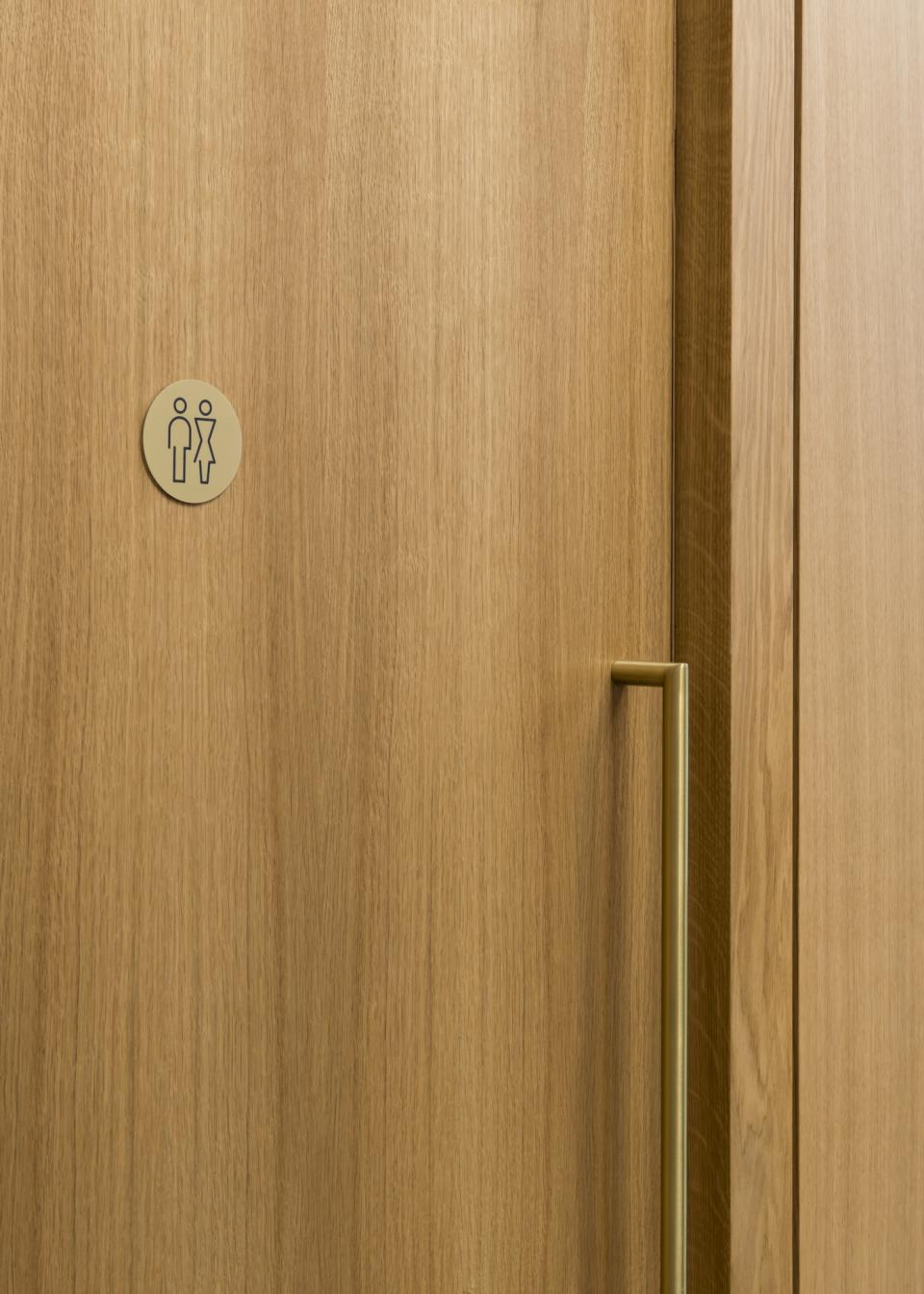 Sign for unisex restroom on wooden door, reflecting sustainable design in Cambridge Central Mosque's architecture.
