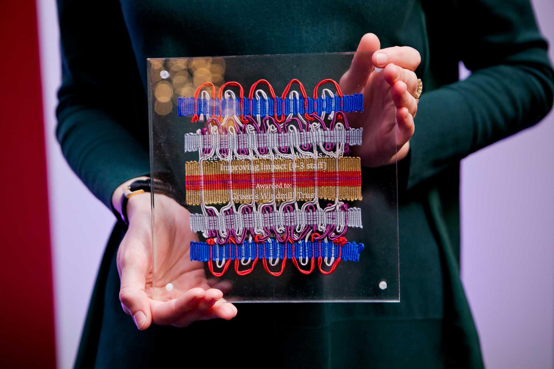 Handcrafted passementerie artwork by Elizabeth Ashdown displayed on a clear plaque, showcasing intricate patterns and vibrant colors.