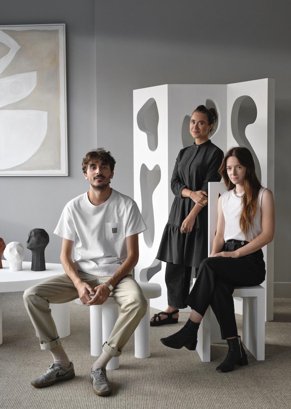 Three designers posing with unique sculptures and furniture during the London Design Festival, showcasing innovative design aesthetics.