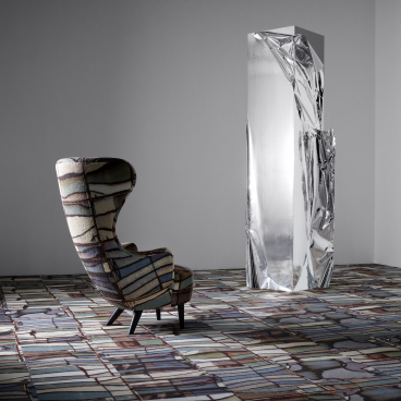 Artful display featuring an upholstered chair and a reflective sculpture on the Industrial Landscape carpet collection by EGE Carpets and Tom Dixon.