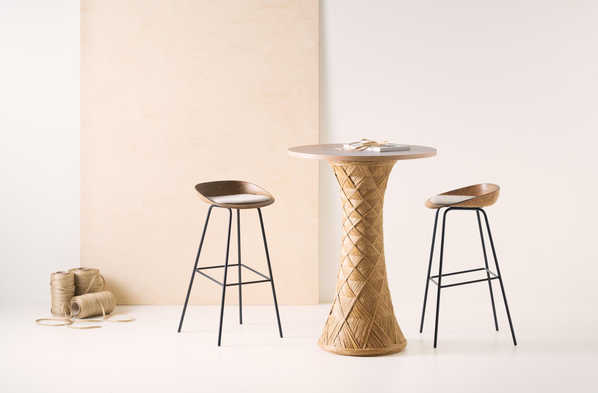 Sustainable wooden table with woven base and stylish stools, showcasing modern design in the Vepa factory environment.